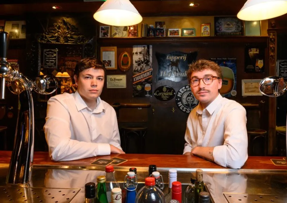 Twee jonge mannen in witte overhemden in een bruine kroeg