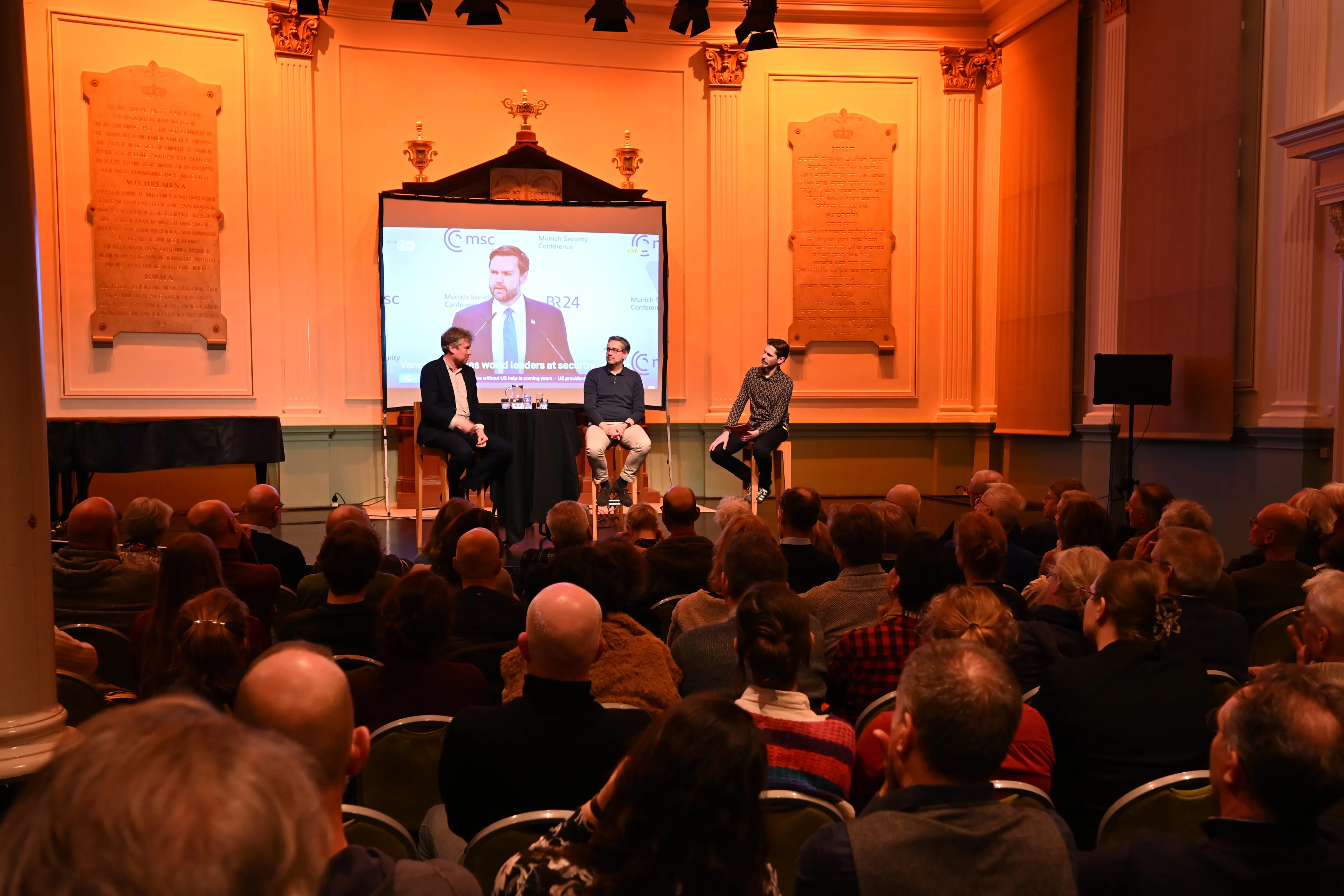 Een programma met bezoekers, met drie mensen op een podium 