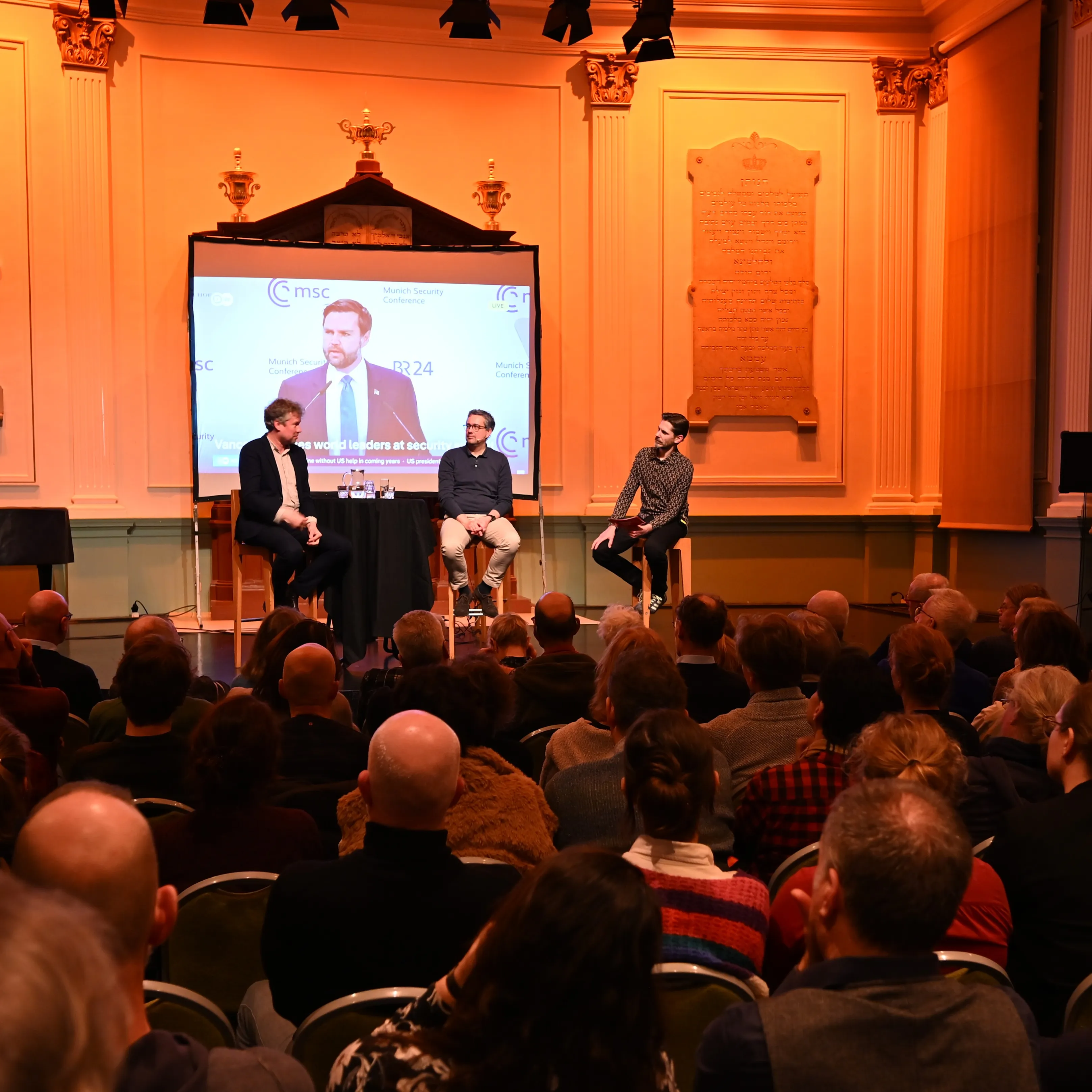 Een programma met bezoekers, met drie mensen op een podium 